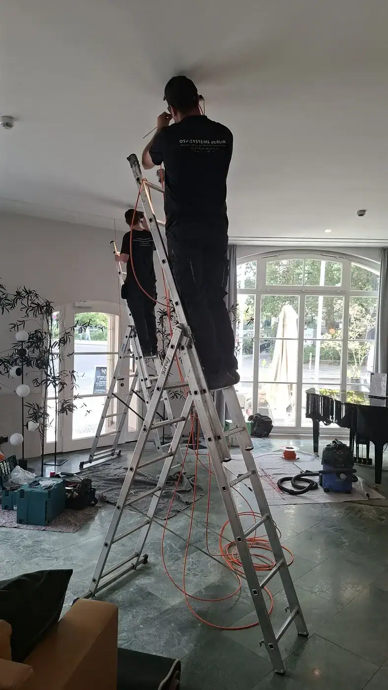 Zwei OSP-Systems Techniker montieren Deckenkameras in einer Hotellobby in Berlin